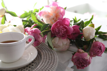 Obraz na płótnie Canvas Beautiful peonies and cup of tea on table, closeup