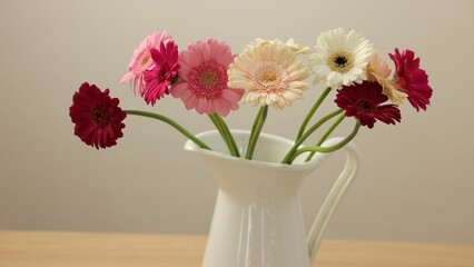 Jug with beautiful gerbera flowers on wooden table