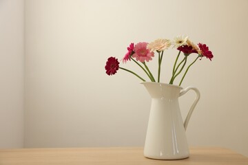 Fototapeta premium Jug with beautiful gerbera flowers on wooden table. Space for text