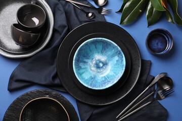 Stylish table setting. Dishware, cutlery and floral decor on blue background, flat lay
