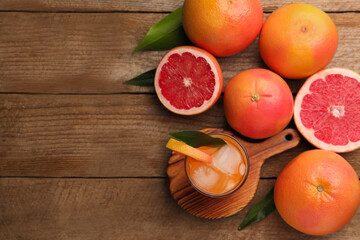 Tasty grapefruit drink with ice in glass and fresh fruits on wooden table, flat lay. Space for text