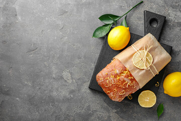Wrapped tasty lemon cake with glaze and citrus fruits on grey textured table, flat lay. Space for text - obrazy, fototapety, plakaty