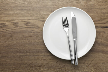 Plate, fork and knife on wooden table, top view. Space for text