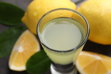 Tasty limoncello liqueur, lemons and green leaves on table, closeup