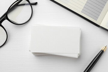 Blank business cards, glasses, notebook and pen on white table, flat lay. Mockup for design