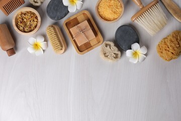 Flat lay composition with different spa products and flowers on light wooden table. Space for text