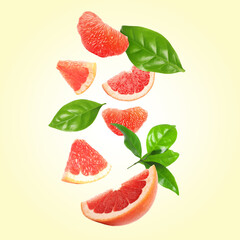 Fresh grapefruit pieces and green leaves falling on light yellow background