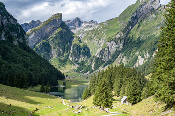 Tourists enjoy the picturesque hiking trail to an alpine lake in a green valley with a mountain...