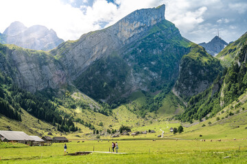 Panoramic view of tourists walking along trail in a green valley with a mountain peak in the...