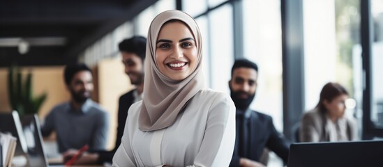 Diverse young colleagues working together in a modern office. Muslim woman smiling after completing a task. - obrazy, fototapety, plakaty