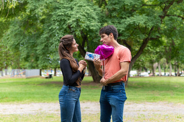 Fototapeta premium Man giving gift to girlfriend, with heart-shaped balloon.