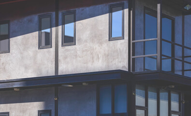 Glass windows on concrete loft wall with black metal external structure of office building in modern industrial style with sunlight and shadow on surface, perspective side view