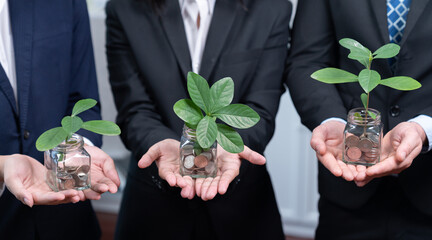 Business people holding money savings jar filled with coins and growing plant for sustainable...