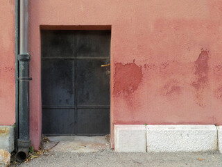 street view of old black metal door against red cement rendered wall with downpipe on building