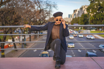 Latino gay male with makeup wearing trendy hat posing on a bridge