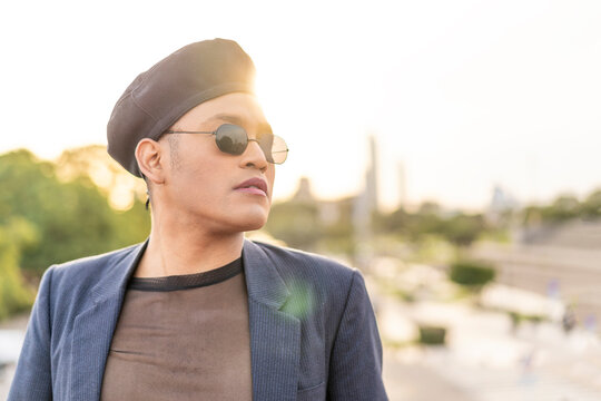 Latino gay male with makeup wearing trendy hat looking aside at sunset