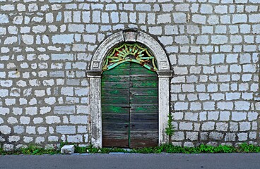 An old wooden green door in the wall of a stone house that has not been opened for a long time