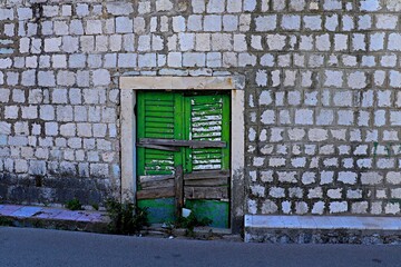 An old wooden green door in the wall of a stone house that has not been opened for a long time,...