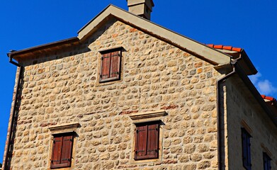Fototapeta na wymiar Stone house with windows closed with wooden shutters against a blue sky