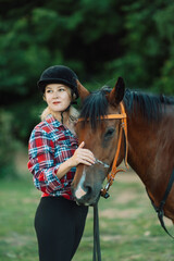 Obraz premium Happy blonde with horse in forest. Woman and a horse walking through the field during the day. Dressed in a plaid shirt and black leggings.