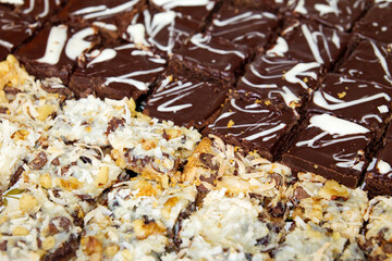 Bakery fresh sliced coconut and chocolate bar cookies and brownie bites sit side by side at a party.