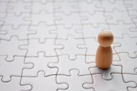A wooden doll on white jigsaw puzzle. Loneliness concept