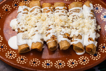 Fried potato tacos with cream and cheese in a Mexican mud dish. Tacos dorados, Mexican food.