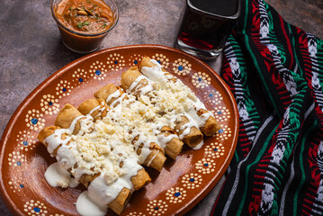 Fried potato tacos with cream and cheese in a Mexican mud dish. Tacos dorados, Mexican food.