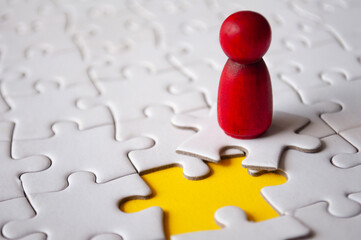 Red wooden doll on top of jigsaw with missing jigsaw puzzle. Hiring and employment concept