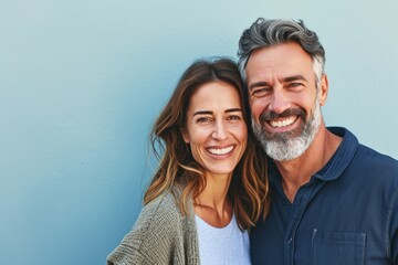 Happy mature couple looking at camera and smiling while standing against blue background - Powered by Adobe