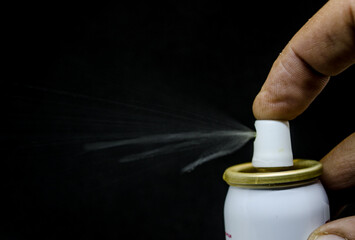 Close up view of a man spraying, A spray can  in a hand on a black background