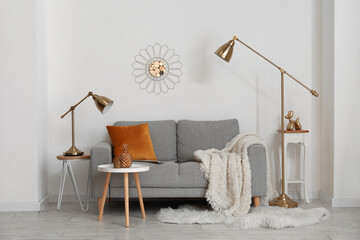 Cozy grey sofa with cushion, lamps and decorative pineapples on table near light wall
