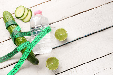 Bottle of water, cucumber and green measuring tape on light wooden background. Diet concept