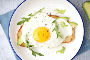 Delicious sandwich with fried egg, avocado and arugula on light background