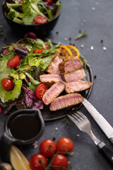 sliced grilled Organic Tuna Steak on black ceramic serving dish with salad on a table