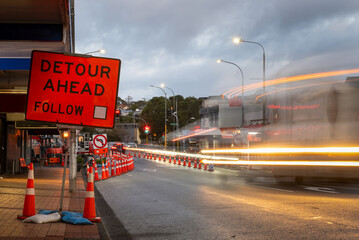 Orange traffic cones on the road. Bus light trails approaching traffic lights. Road works in...