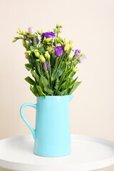 Jug with eustoma flowers on table near white wall