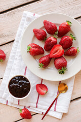 Plate with fresh strawberries and jam on white wooden background