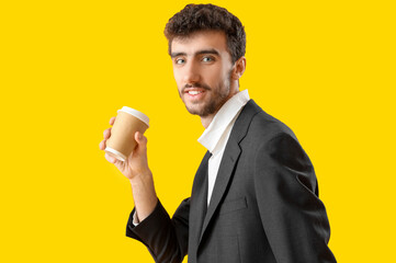 Young man in suit with cup of coffee on yellow background