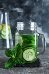 Mason jar and bottle of infused water with cucumber slices on grey table