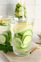 Board and glasses of infused water with cucumber slices on white table