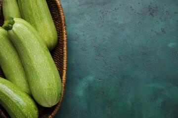 Wicker basket with fresh zucchini on green background