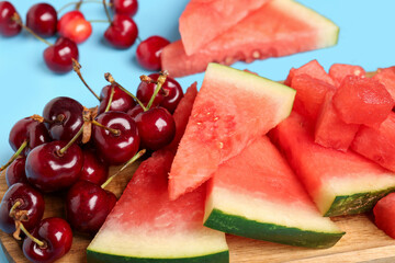 Board with pieces of fresh watermelon and cherries on blue background