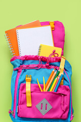Backpack with blank notebook and stationery on green background