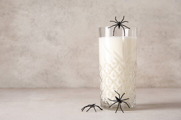Glass of milk and spiders for Halloween on light background