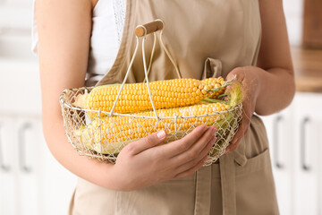 Woman holding basket with fresh corn cobs in kitchen