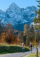 Fototapeta na wymiar Women walking on a trail under snowy mountain peaks on autumn day