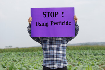 Text Stop Using Pesticide on paper poster, held by farmer at garden. Concept, campaign for calling...