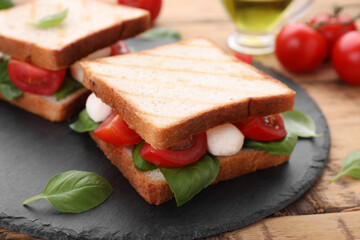 Delicious Caprese sandwiches with mozzarella, tomatoes, basil and pesto sauce on wooden table, closeup