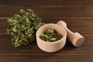 Mortar and pestle with dry parsley on wooden table